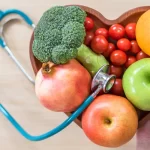 Frutas y verduras frescas en un plato con forma de corazón y un estetoscopio alrededor