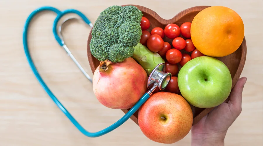 Frutas y verduras frescas en un plato con forma de corazón y un estetoscopio alrededor